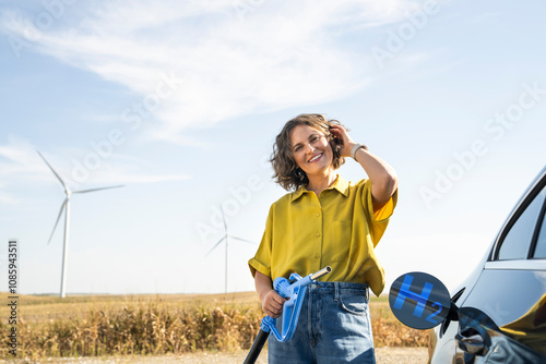 Woman holds a hydrogen fueling nozzle. Refueling car with hydrogen fuel. Wind turbines in the background.