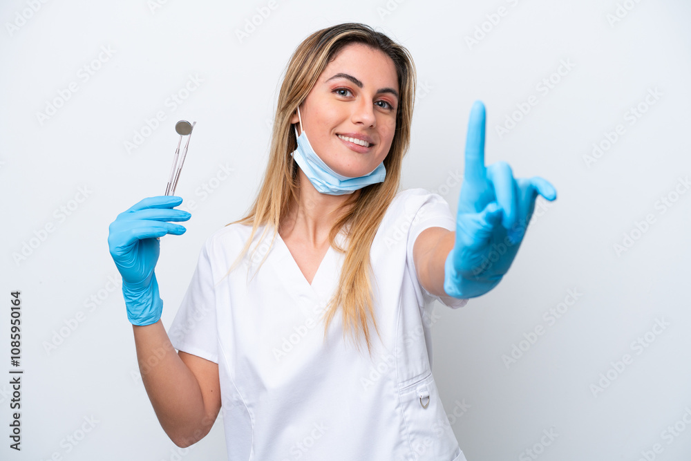 Dentist woman holding tools isolated on white background showing and lifting a finger Dentist woman holding tools isolated on white background showing and lifting a finger