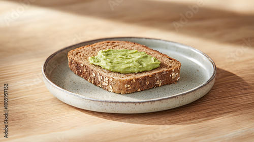 A single slice of whole grain bread with avocado spread arranged neatly on a small ceramic plate.