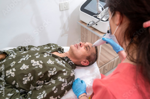 woman in a red shirt is treating a man's face with a device