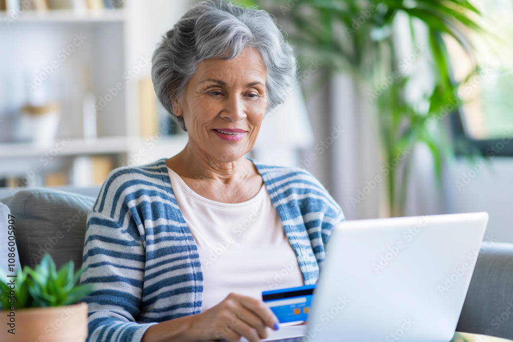 Senior Woman holding credit card while using her laptop in cozy living room with greenery. Perfect for themes of online shopping, convenience, and independent living. Senior Woman holding credit card while using her laptop in cozy living room with greenery. Perfect for themes of online shopping, convenience, and independent living.