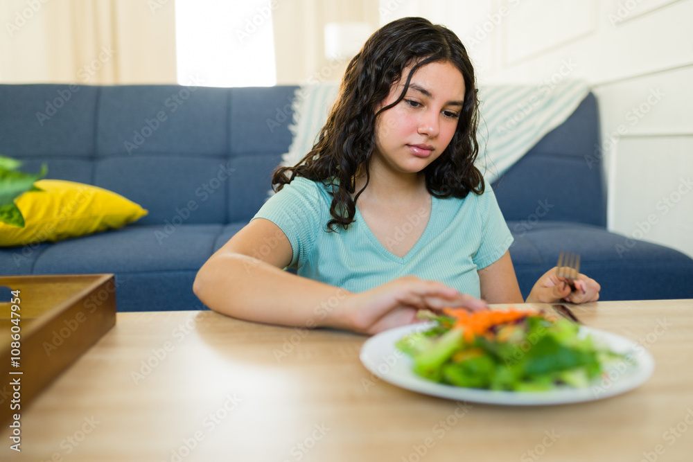 Teen girl with eating disorder and health problems rejecting fresh salad during home lunch Teen girl with eating disorder and health problems rejecting fresh salad during home lunch