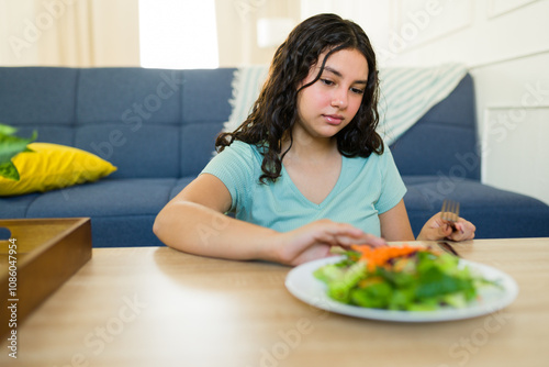 Teen girl with eating disorder and health problems rejecting fresh salad during home lunch