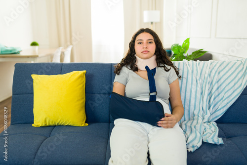 Frustrated teenage girl in neck brace and arm sling resting on sofa at home, recuperating from injury photo