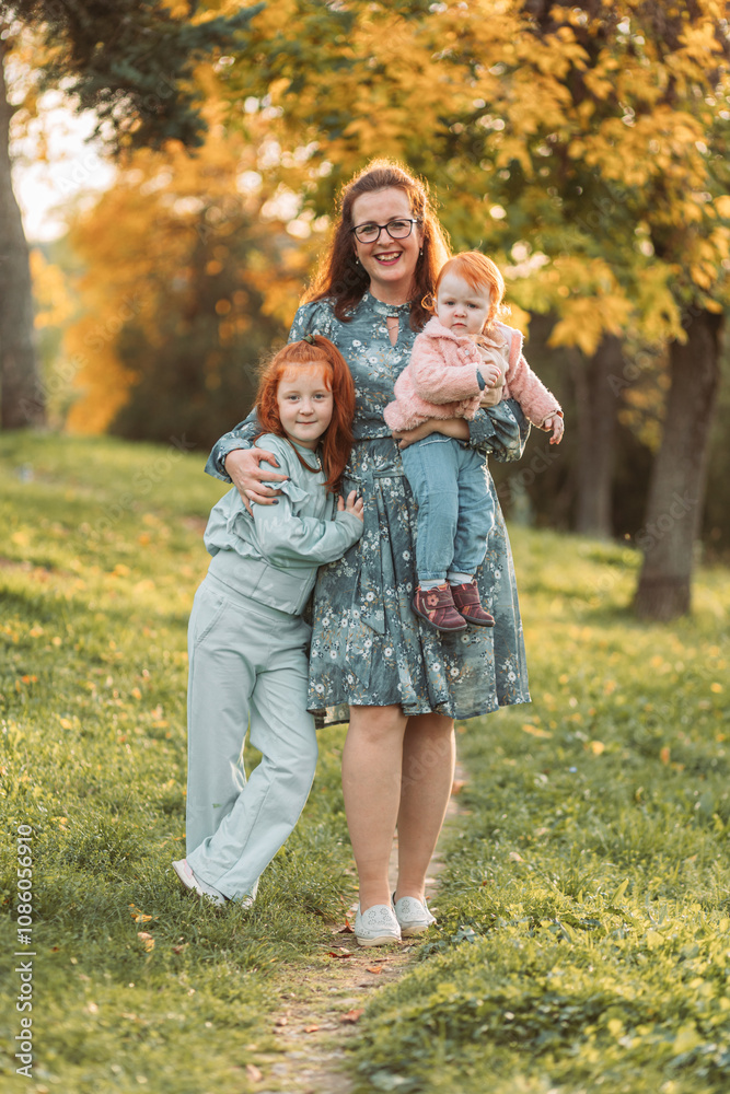 Fototapeta premium Young mom with her little ginger daughters. Mothers day, connection