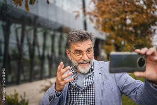 Senior man explain something on video call in front modern building