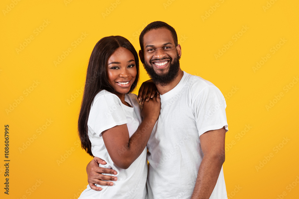 Happy Loving Family. Portrait of handsome millennial black man embracing his beautiful beloved woman, couple in casual white t-shirts standing and posing isolated over yellow orange studio background Happy Loving Family. Portrait of handsome millennial black man embracing his beautiful beloved woman, couple in casual white t-shirts standing and posing isolated over yellow orange studio background