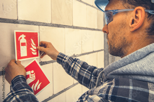 Konstfotografi Worker Installing Fire Safety Signs on a Construction Site During Daylight Hours