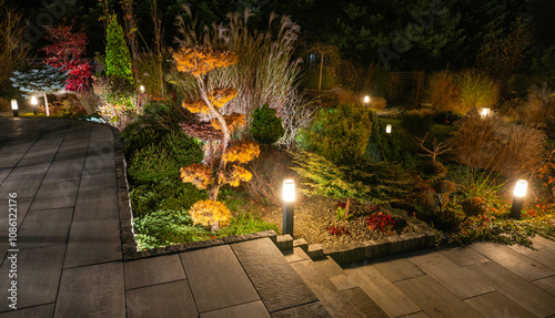 Fototapeta Naklejka Na Ścianę i Meble -  Beautifully Lit Garden Pathway at Night Showcasing Colorful Trees and Lush Foliage