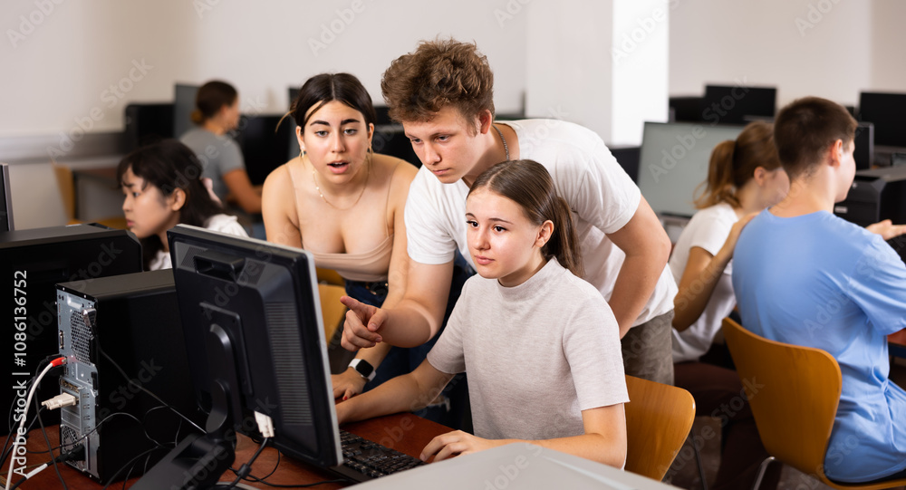Serious teenagers helping to the female classmate while she is learning computer science in the class Serious teenagers helping to the female classmate while she is learning computer science in the class