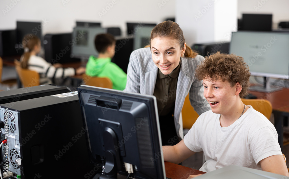 Female teacher and her student, teenage boy, looking at monitor of PC during computer science lesson and smiling. Female teacher and her student, teenage boy, looking at monitor of PC during computer science lesson and smiling.