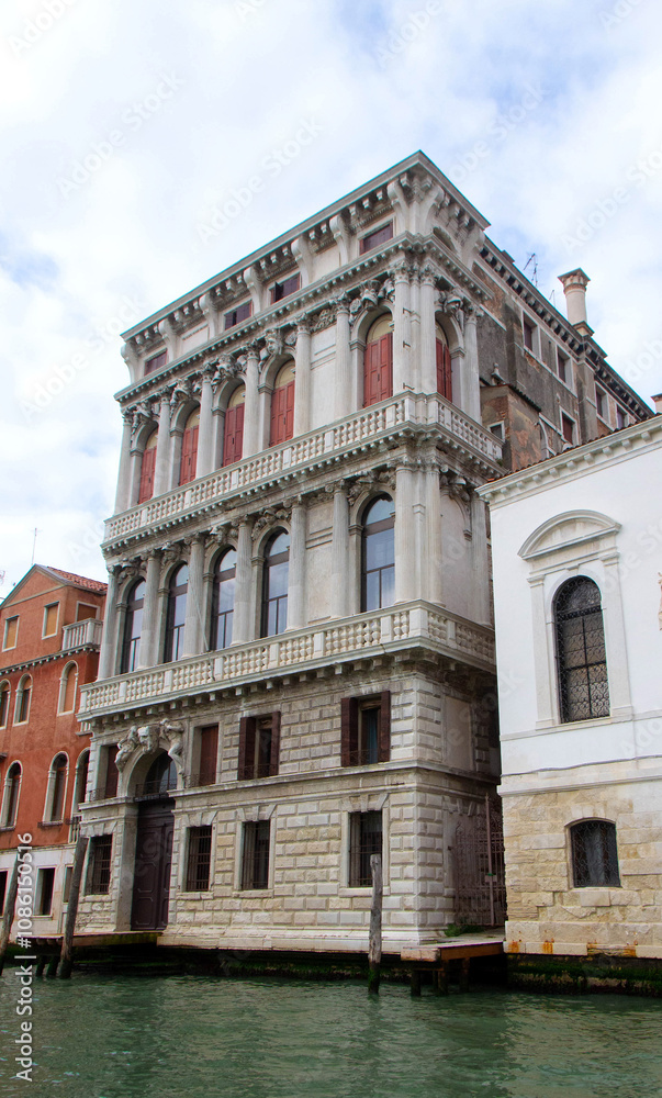 A view of historic Venetian buildings along the Grand Canal, showcasing classic Italian architecture. The iconic canal waters reflect the facades, with boats and gondolas adding to the charm of Venice
