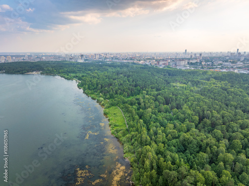 Big lake with green shores in bright sun light and city on horizon, aerial landscape. Recreation concept. Aerial view photo