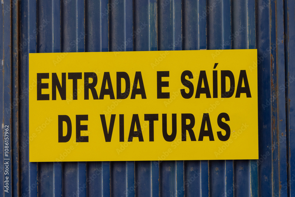 Yellow sign indicating vehicle entrance and exit in portuguese on blue metal door Yellow sign indicating vehicle entrance and exit in portuguese on blue metal door