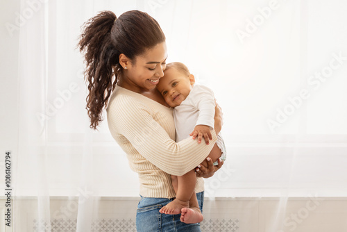 Loving African American Mother Holding Baby Cuddling Toddler In Arms Enjoying Motherhood And Child Care Standing Indoors. Happy Motherhood Moments, Mom And Infant's Bond Concept photo