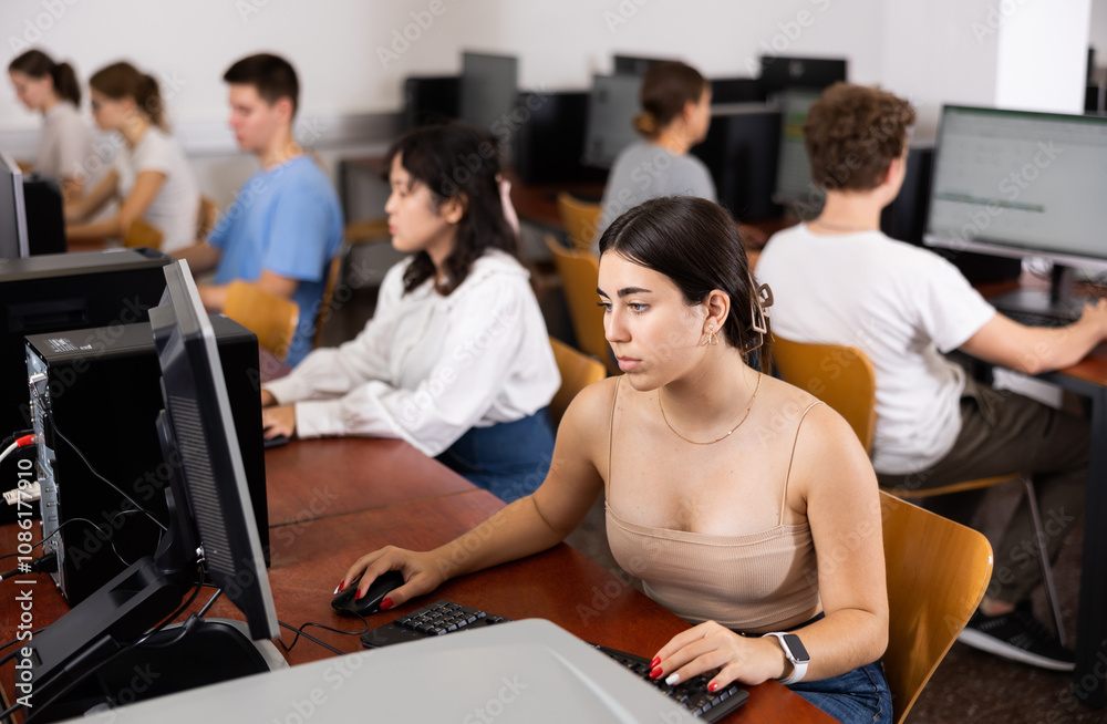 Group of young smart students studying together in university computer class. Focus on concentrated girl Group of young smart students studying together in university computer class. Focus on concentrated girl