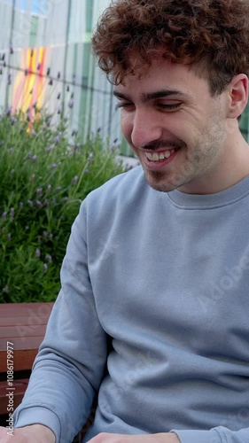 Vertical HD video of young happy student man using laptop at university campus. Smiling millennial male sitting on table while working on computer outdoors. Education and college people concept. photo