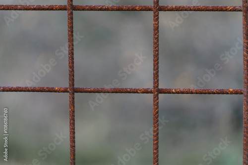 Detail of rusty steel or iron metal mesh used as fence with green blurry vegetation as background