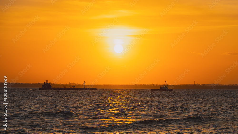 A cargo ship is being towed by a tugboat during sunset. A cargo ship is being towed by a tugboat during sunset.
