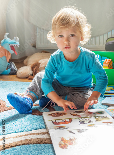 Obraz na płótnie Cute little child boy reading books about animals, sitting on the floor, at home w salonie