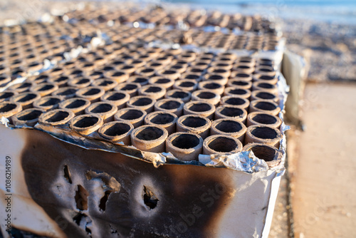 Close-up of charred firework tubes left on a sandy beach, the aftermath of a coastal celebration under the sun. photo