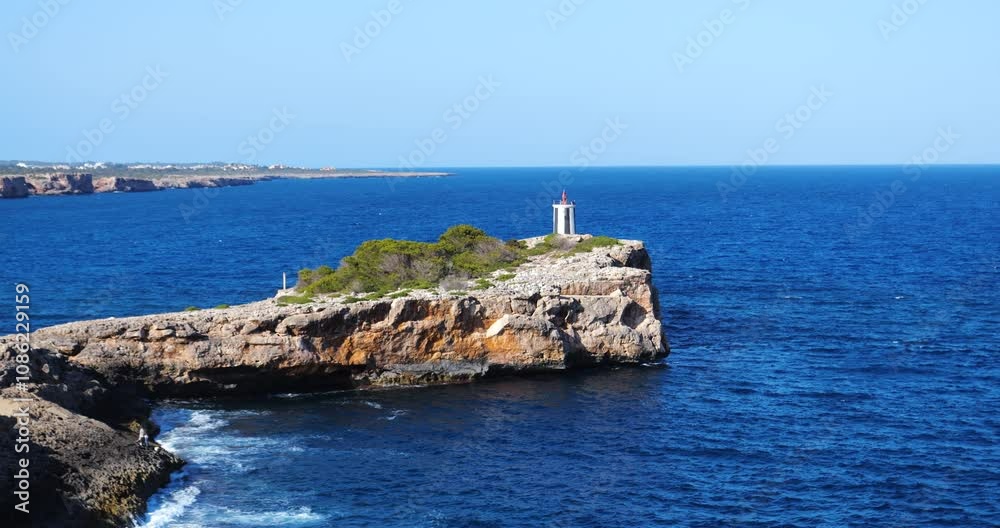 Aerial establishing shot of Far do es Morro de Sa Carabassa lighthouse on a rugged cliff by the deep blue sea in Porto Cristo, Mallorca, Spain, on a clear day Aerial establishing shot of Far do es Morro de Sa Carabassa lighthouse on a rugged cliff by the deep blue sea in Porto Cristo, Mallorca, Spain, on a clear day