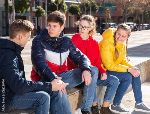 Portrait of four teenagers having friendly discussion during gathering outdoors on sunny spring day photo