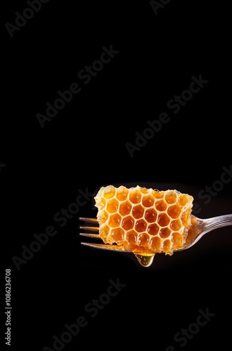 honeycomb on an antique fork. The honeycomb glistens with honey, and a few drops noticeably flow down. on a black background photo