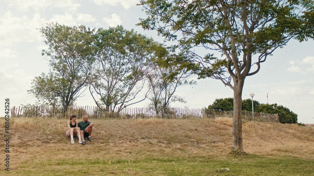 Young athletic couple relaxing in the park in summer sitting on the grass Young athletic couple relaxing in the park in summer sitting on the grass
