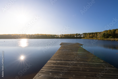 A wooden pier sits on a lake, with the sun reflecting off the water