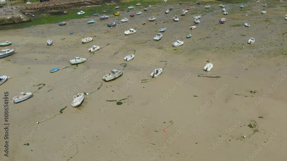 Small boats rest anchored on the exposed sandy shoreline at low tide in a coastal village. The colorful houses in the background highlight the charming simplicity of Brittany, France. Small boats rest anchored on the exposed sandy shoreline at low tide in a coastal village. The colorful houses in the background highlight the charming simplicity of Brittany, France.