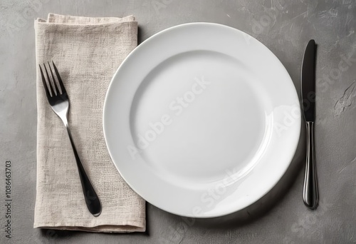 A clean, white plate with a folded cloth napkin on a concrete surface viewed from above