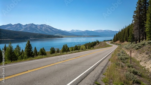 A peaceful scene of an empty asphalt road running alongside a lake or ocean with mountains visible in the distance under a clear blue sky, serenity, ocean, calmness