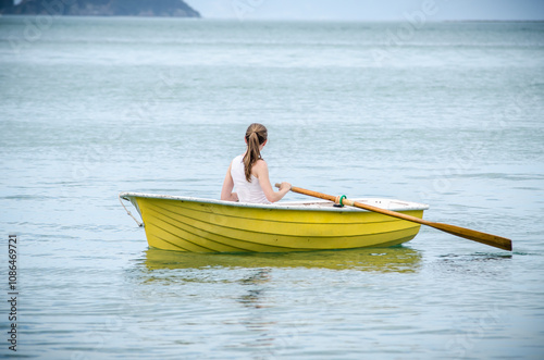 Young woman rowing a small yellow boat on calm water