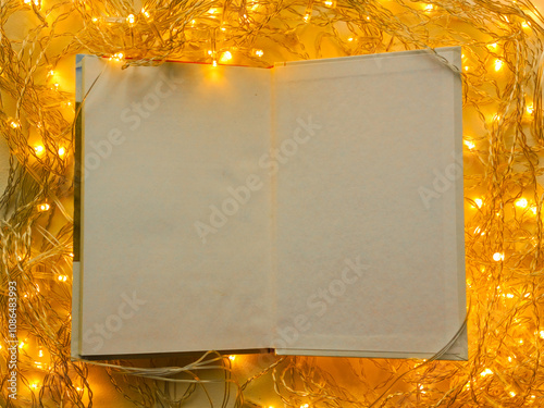 An open notebook with white pages on a background of bright yellow garland lights. Background, place for text. Drawing up new goals is a concept. photo