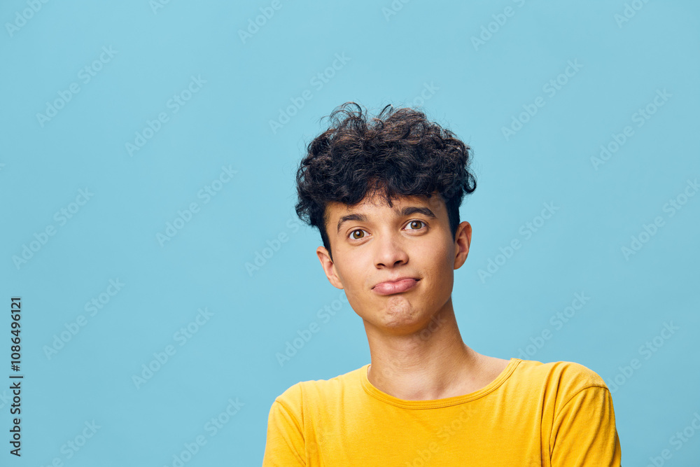 Portrait of a young man with curly hair making a thoughtful expression against a light blue background, wearing a yellow shirt, conveying curiosity and contemplation in a cheerful ambiance Portrait of a young man with curly hair making a thoughtful expression against a light blue background, wearing a yellow shirt, conveying curiosity and contemplation in a cheerful ambiance