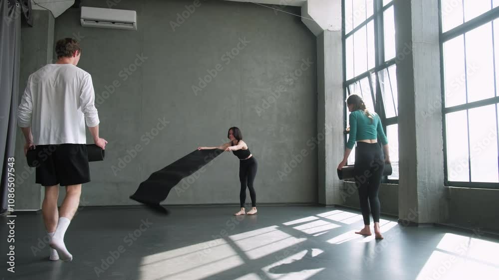 Yoga class. Sport training. Group people in activewear with athletic woman instructor unroll fitness mat before workout exercise in gym studio indoors. Yoga class. Sport training. Group people in activewear with athletic woman instructor unroll fitness mat before workout exercise in gym studio indoors.
