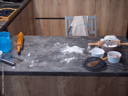 Cookie cutters, rolling pins, flour, eggs, and other baking ingredients are scattered on a messy kitchen counter, suggesting someone is actively preparing cookie dough