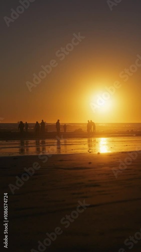 camera right to left tracking of people at ocean sunset on reflective wet sand at waters edge vertical video