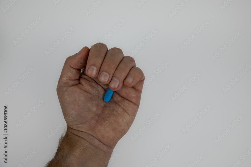 Almost closed caucasian male fist with a blue pill in the palm. Hand against a white background. Concept for regular medication use. Almost closed caucasian male fist with a blue pill in the palm. Hand against a white background. Concept for regular medication use.