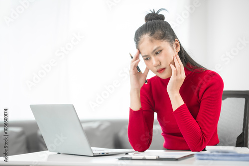 Obraz na plátně A businesswoman sits at her desk, stressed and anxious while looking at her laptop