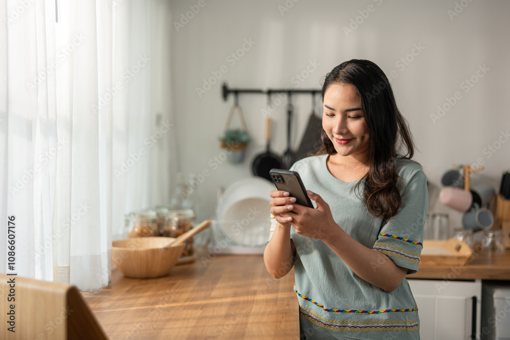 Asian attractive woman chatting on mobile phone device in kitchen at home. Asian attractive woman chatting on mobile phone device in kitchen at home.