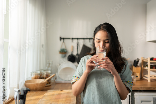 Bilde på lerret Asian young attractive woman drink a glass of water in kitchen at home