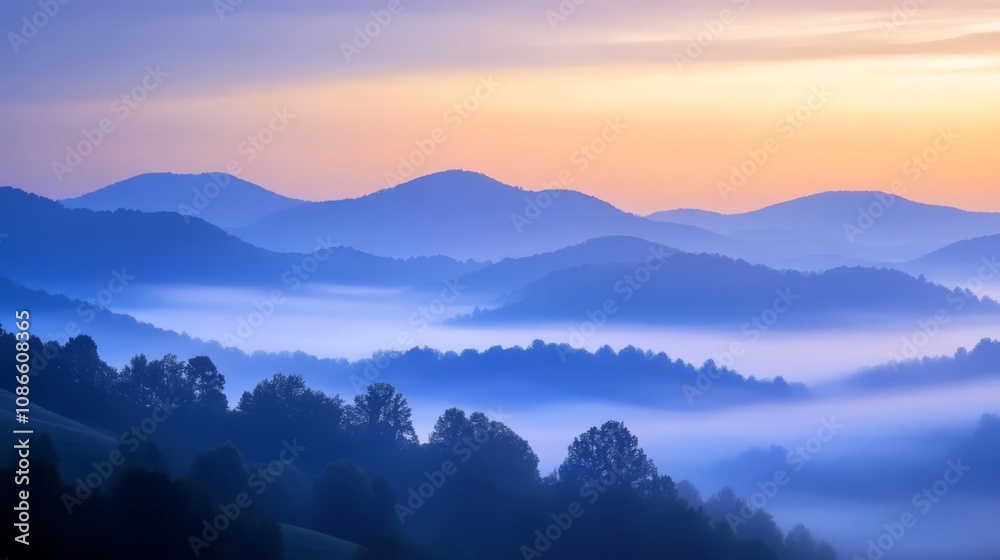 Fototapeta premium Misty sunrise over rolling hills with a soft, blue and orange sky.