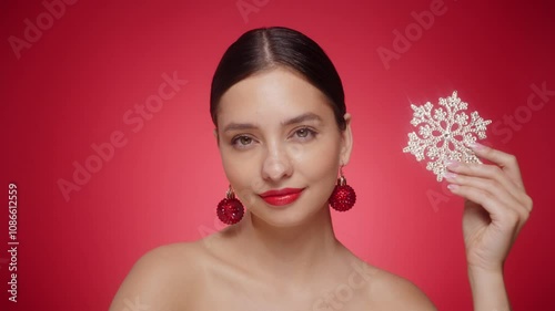 Beautiful young woman with red lipstick, showing glowing snowflake, near face and smiling, isolated on a red background. Christmas holidays concept. Slow motion video