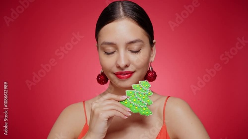 Beautiful young woman with cookie Christmas tree isolated on red background. Christmas or New Year festivities. Holiday and Party. Slow motion video