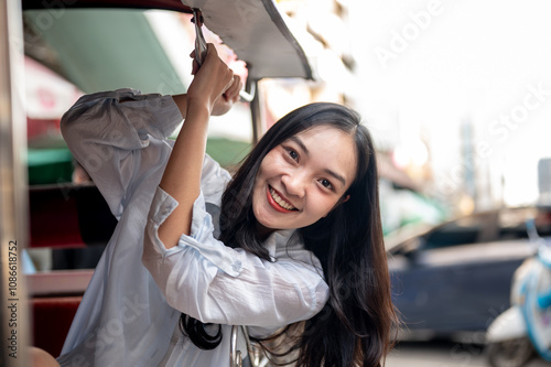Photography A beautiful Asian female tourist enjoying a ride in a tuk-tuk in Thailand, looking at the camera