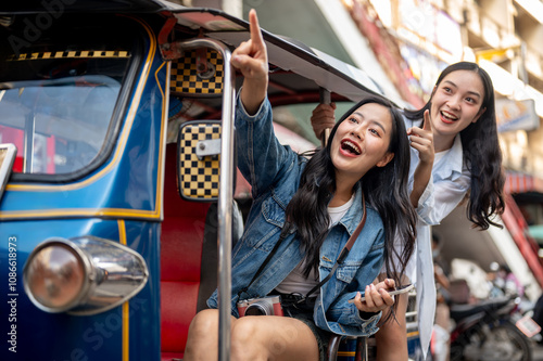 Photography Two excited Asian girl tourists enjoy a ride in a tuk-tuk in Thailand, pointing at the view