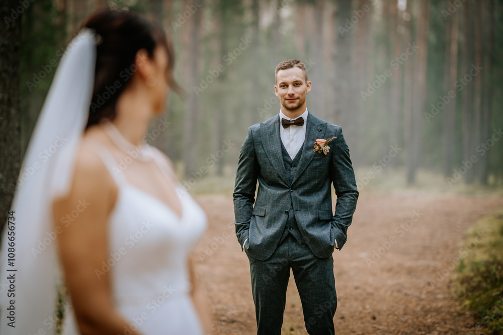 Groom in a tailored suit stands confidently in a forest, gazing at the bride in soft focus, creating a romantic outdoor wedding atmosphere.. Groom in a tailored suit stands confidently in a forest, gazing at the bride in soft focus, creating a romantic outdoor wedding atmosphere..