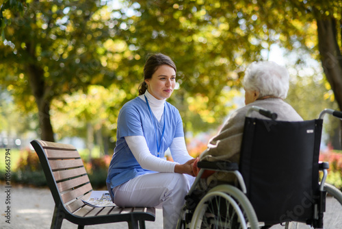 Disabled elderly woman in wheelchair holding hands with her nurse, talking about her problems.